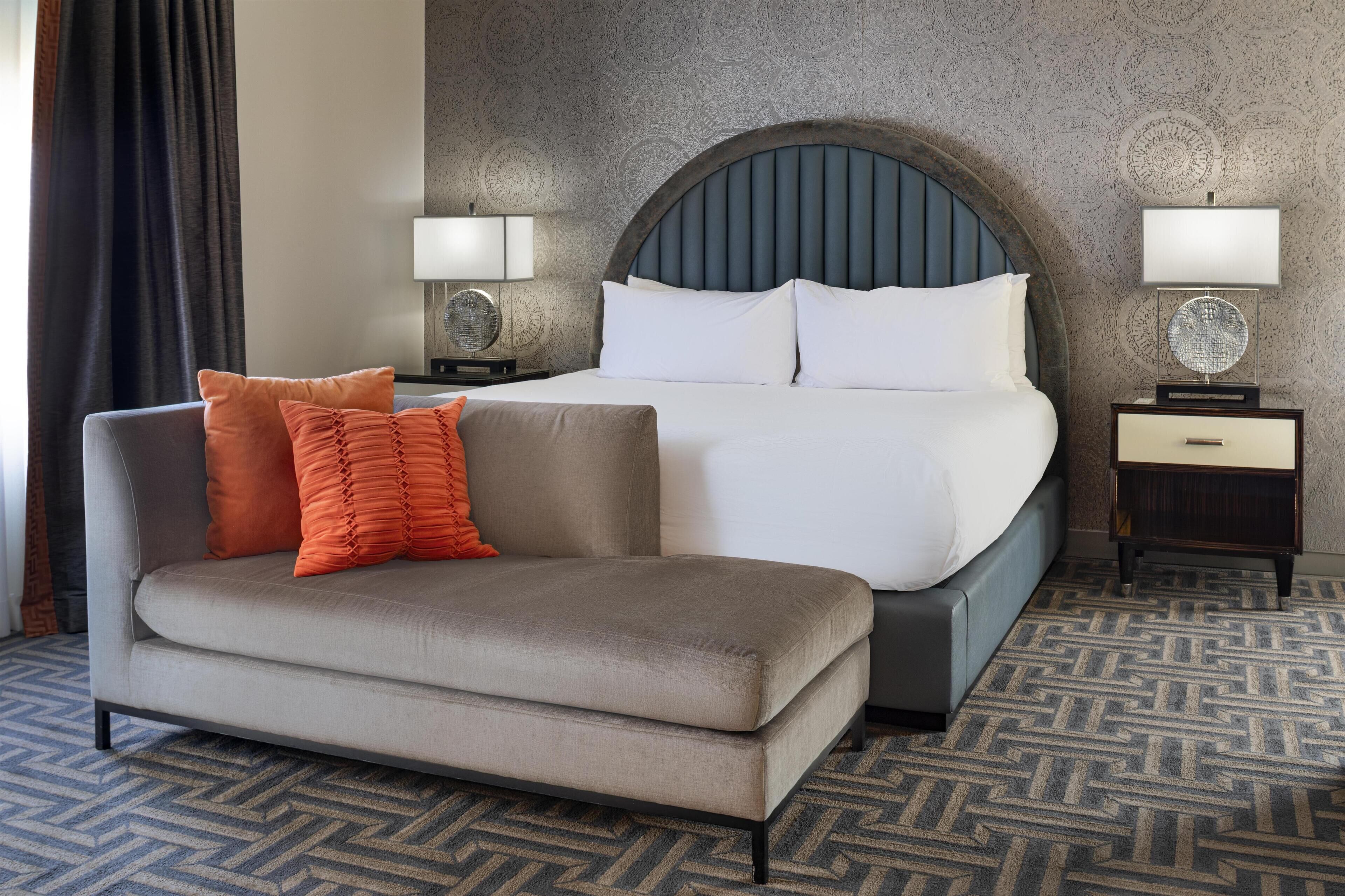 A hotel room with a bed, a sofa, two bedside tables with lamps, and a patterned carpet.