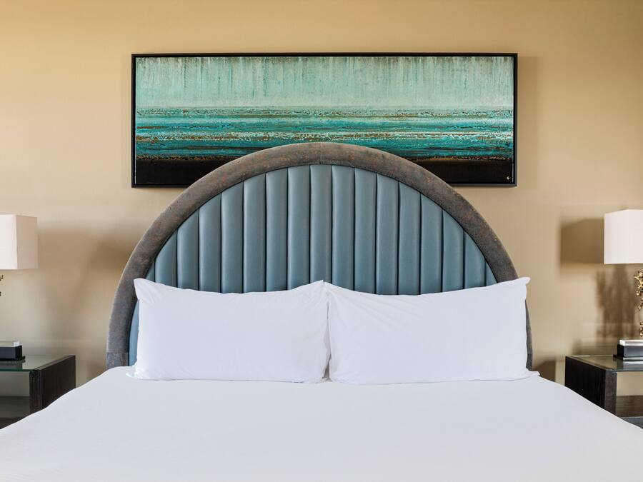 A hotel room with a bed, a headboard, two bedside tables, and a painting on the wall.