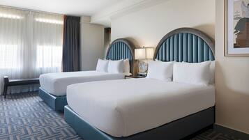 A hotel room with two beds, a bench, a nightstand with a lamp, and a framed picture on the wall.