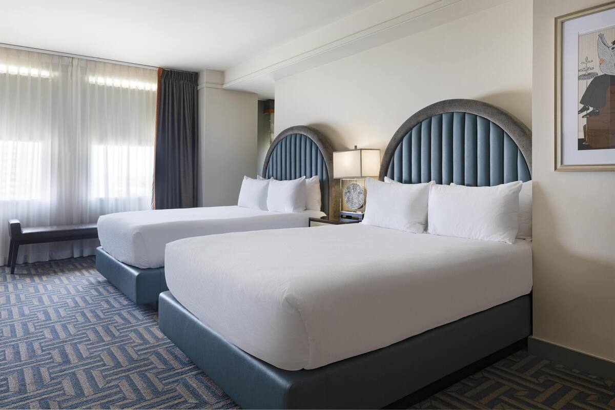 Habitación de hotel con dos camas, un banco, una lámpara y un cuadro en la pared.