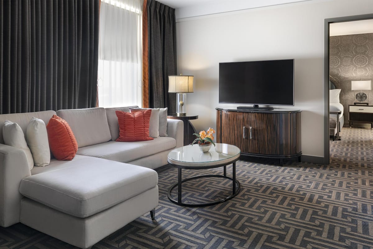 Una habitación de hotel moderna con sofá, mesa de centro, televisión de pantalla plana y alfombra estampada.