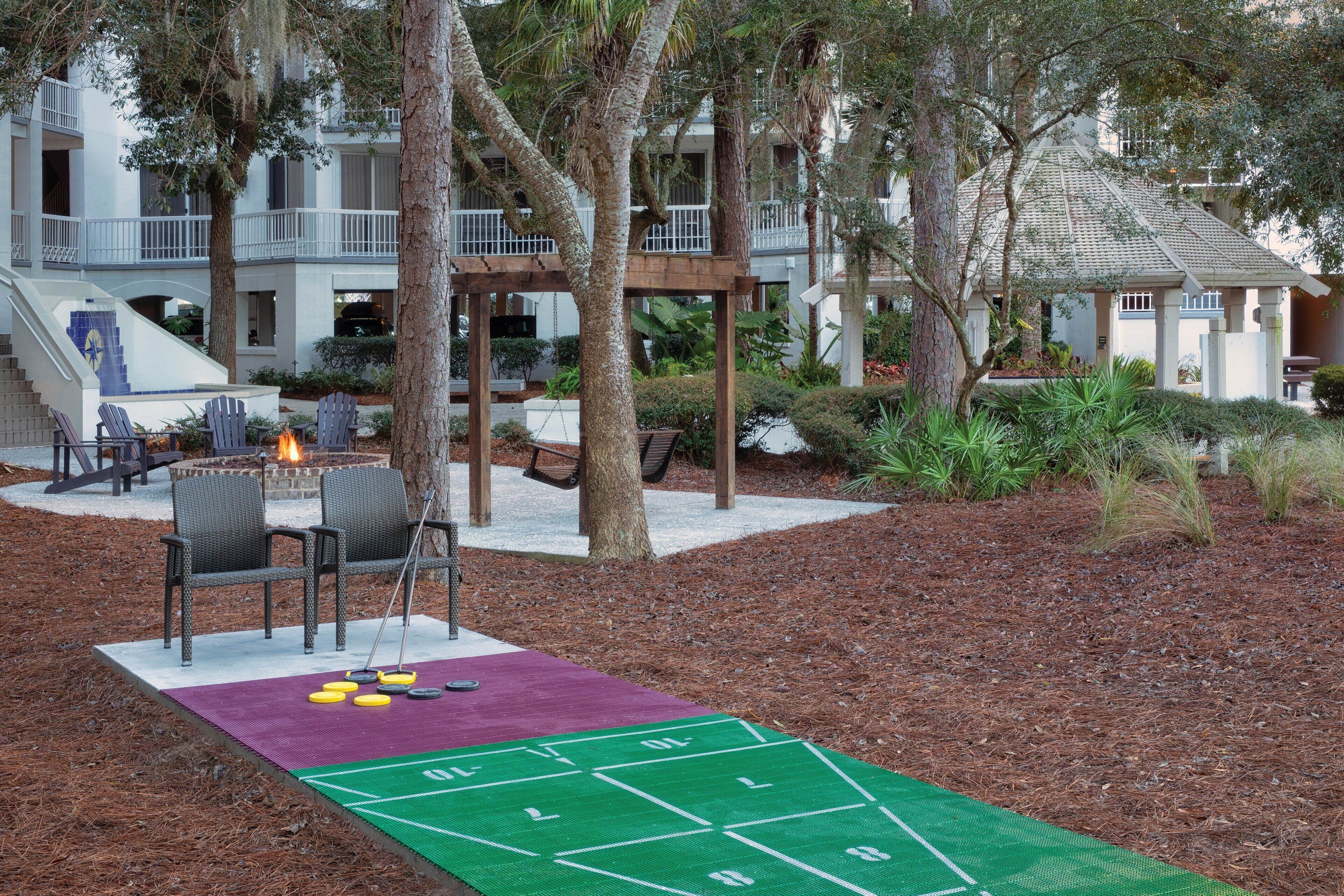 A courtyard with a shuffleboard table, outdoor seating, and a fire pit.