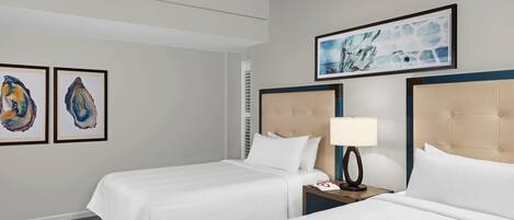 A hotel room with two beds, a ceiling fan, artwork on the walls, and a nightstand with a lamp.