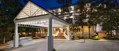 A hotel entrance with a covered walkway, a staircase, and a landscaped area with trees and shrubs.