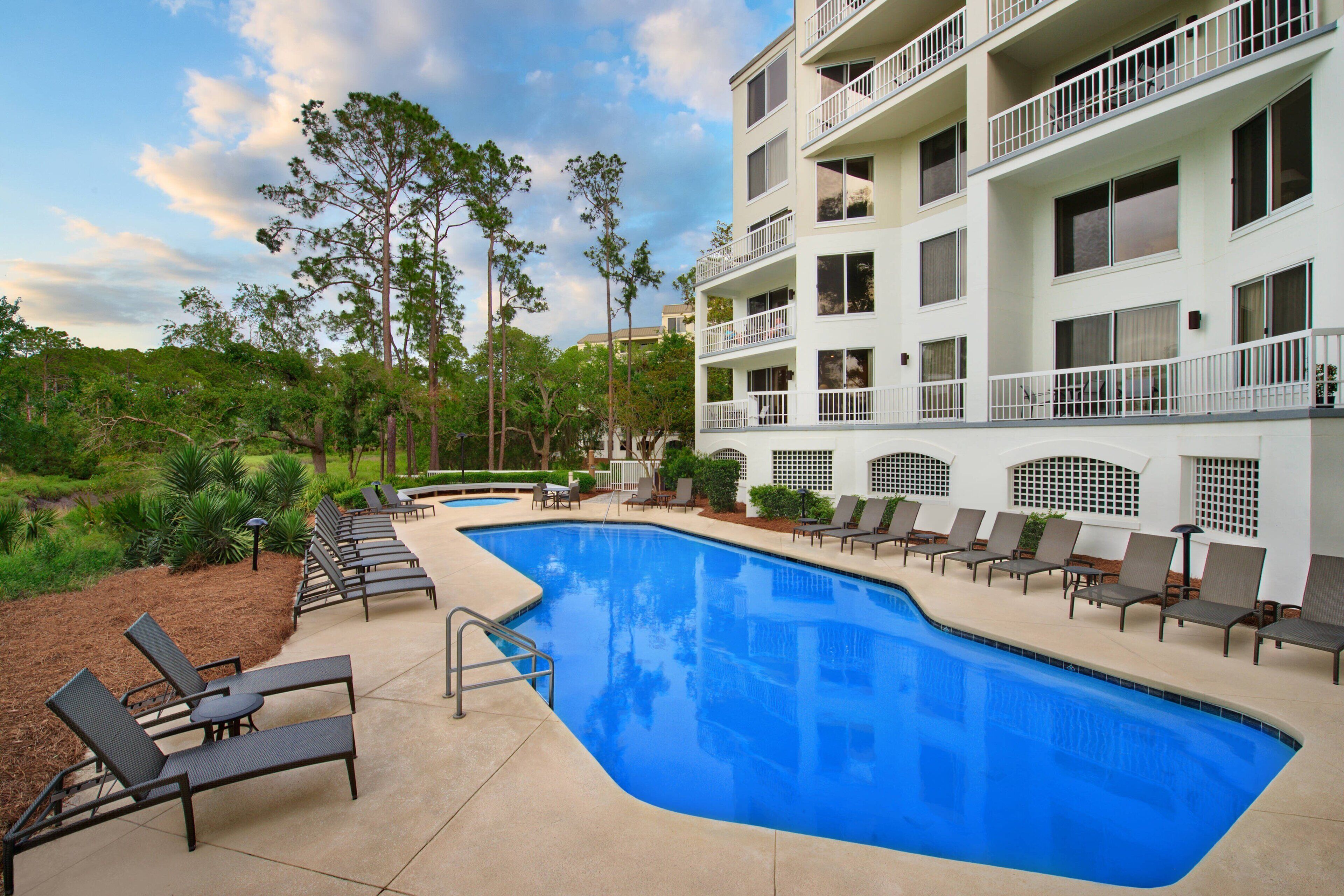 A swimming pool with lounge chairs and a building with balconies.