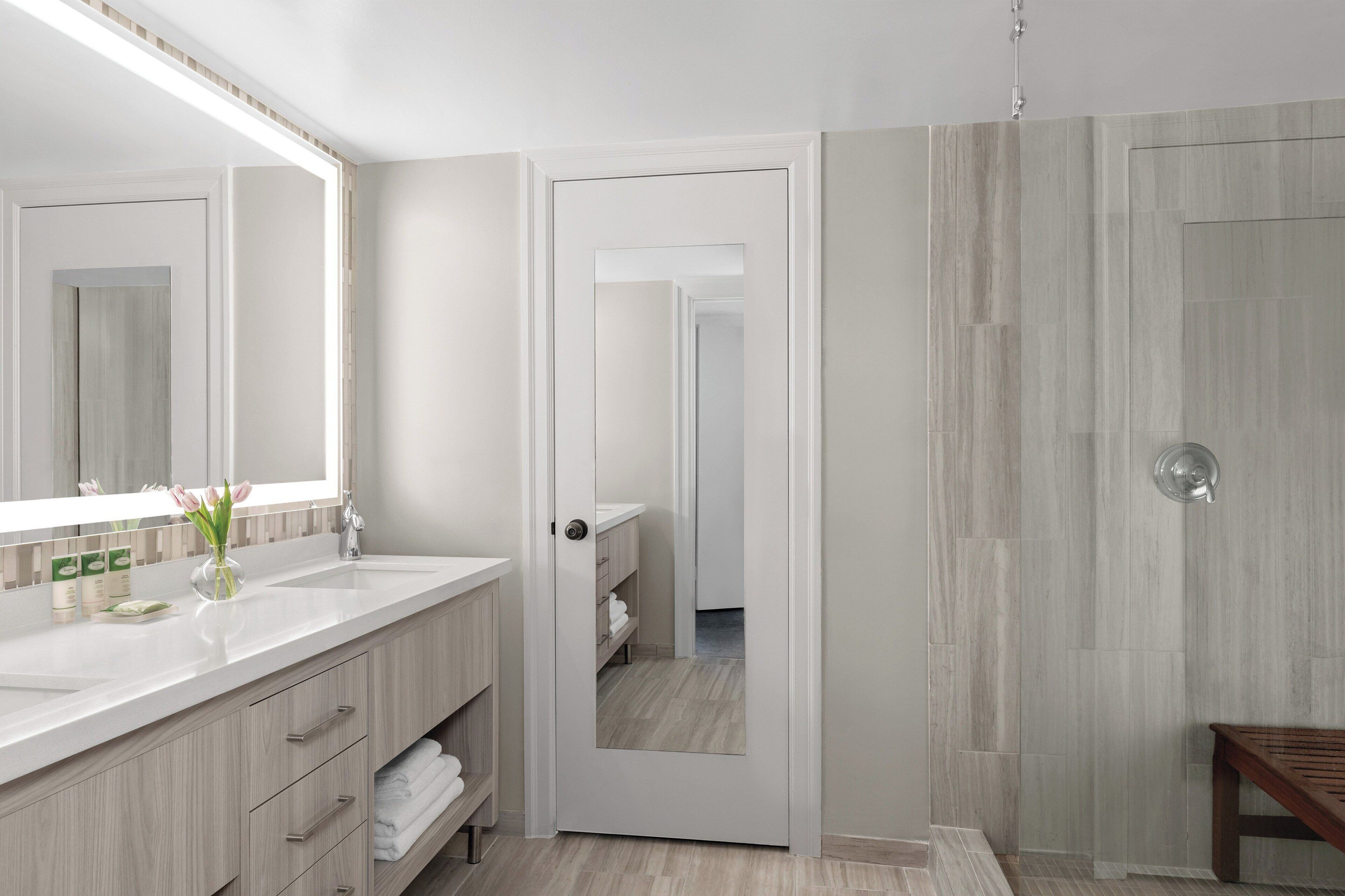 A modern bathroom with a large mirror, a white sink, and a wooden vanity.