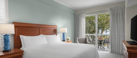 A hotel room with a large bed, two bedside tables with lamps, a TV, and a balcony with a table and chairs.