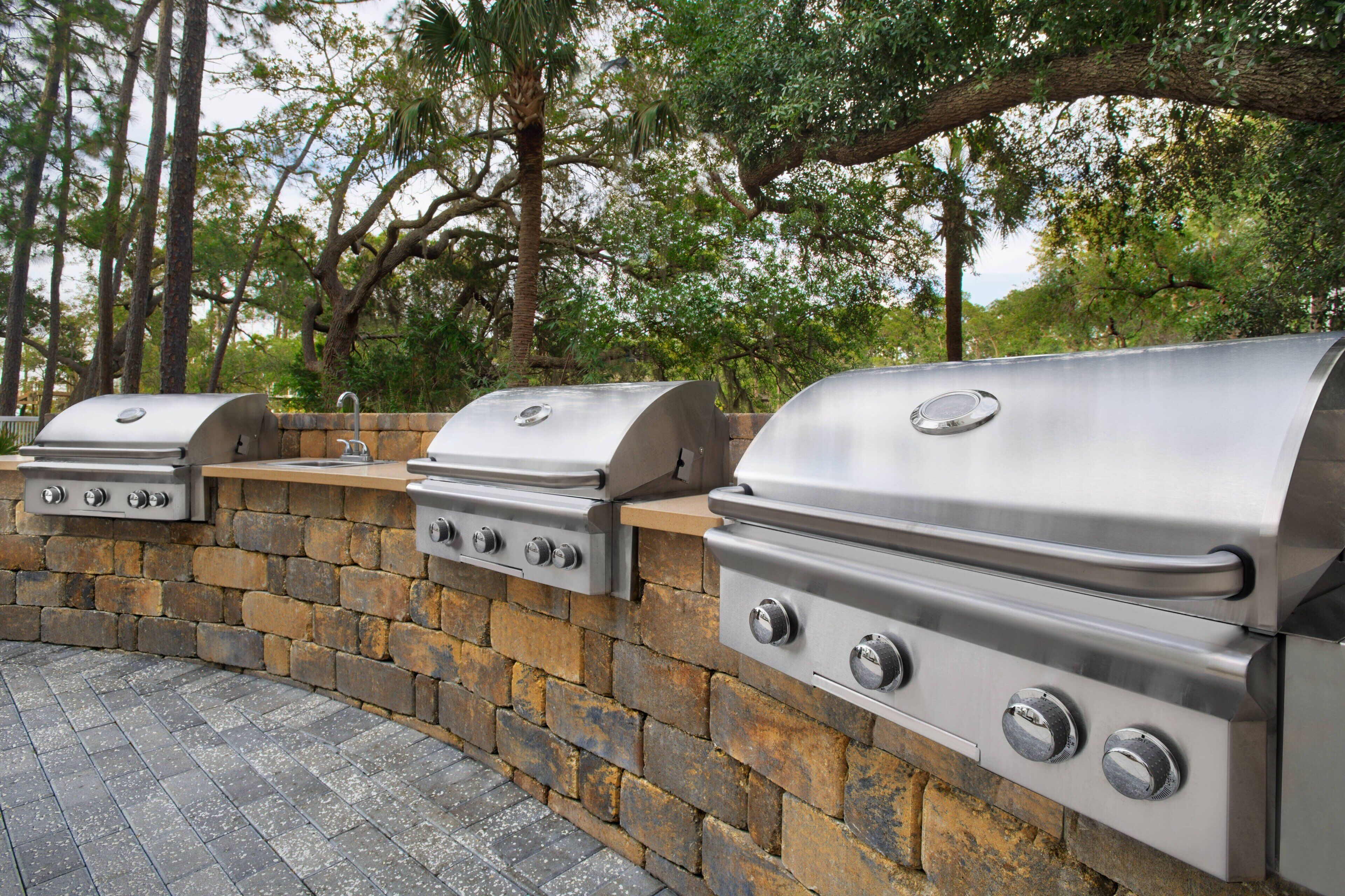 A stone wall with three stainless steel barbecue grills.