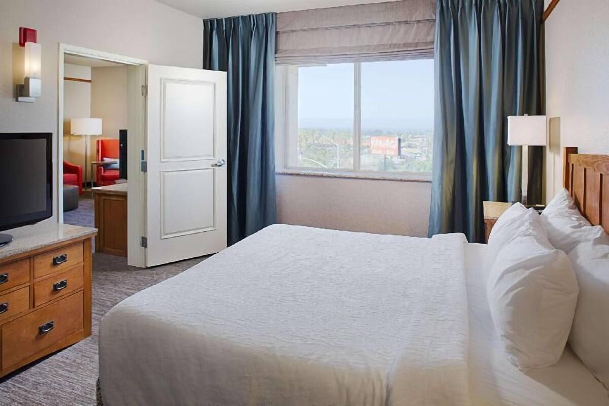A hotel room with a bed, a TV, a desk, a chair, and a window with curtains.