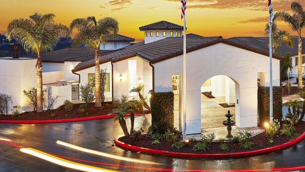 A hotel entrance with a white facade, palm trees, and a sunset sky.