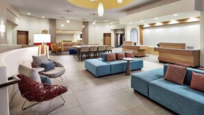A hotel lobby with seating areas, a reception desk, and a modern chandelier.