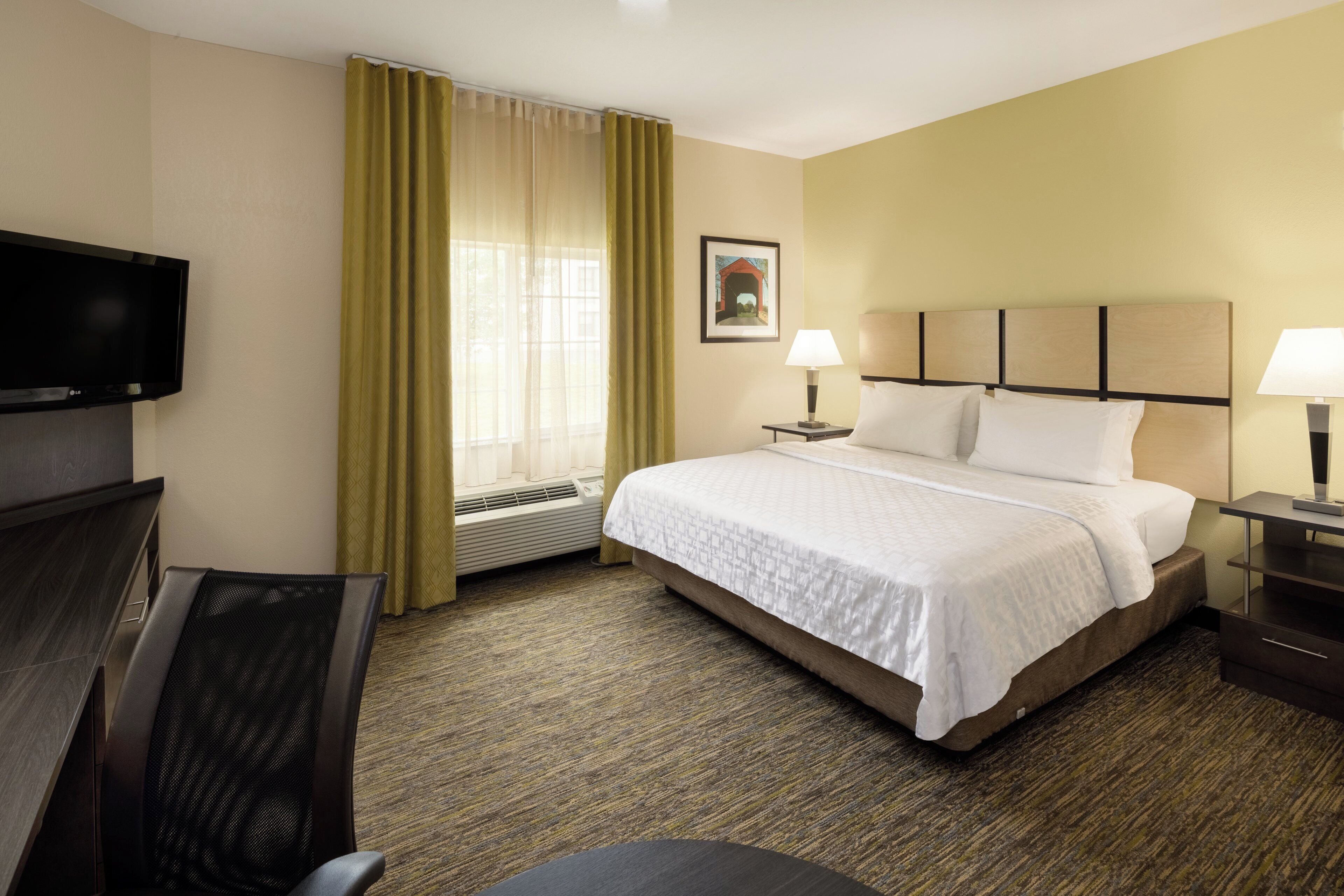 A hotel room with a bed, two bedside lamps, a TV, a desk, and a chair.