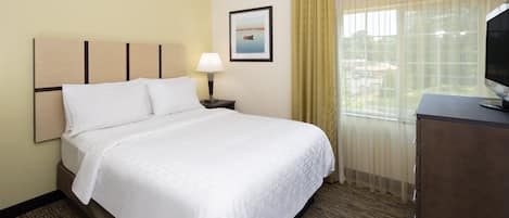 A hotel room with a bed, a nightstand, a lamp, a television, and a window with curtains.