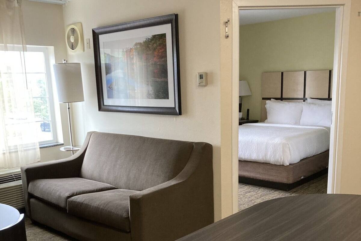 Una habitación de hotel con sofá, cama, escritorio y un cuadro en la pared.