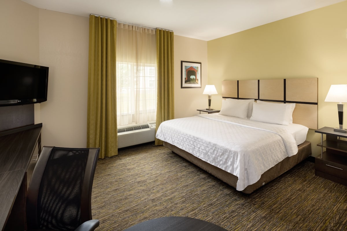 Una habitación de hotel con una cama, dos lámparas de noche, un televisor, un escritorio y una silla.