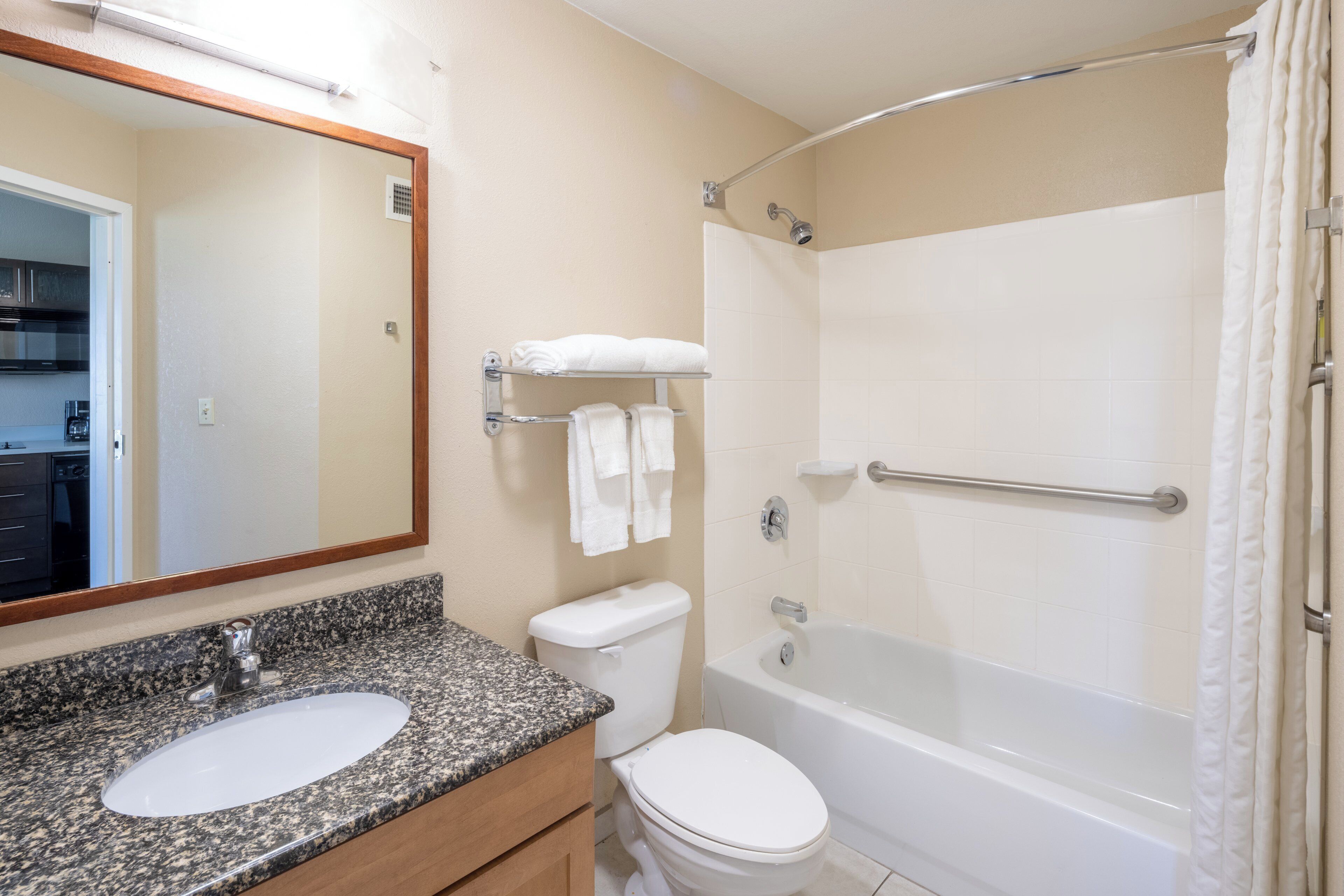 Une salle de bain avec un lavabo sur un plan de travail en granit, des toilettes, une baignoire avec un rideau de douche et un miroir au-dessus du lavabo.