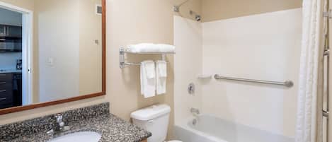 A bathroom with a granite countertop sink, a toilet, a bathtub with a shower curtain, and a mirror above the sink.