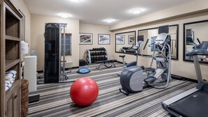 Un gimnasio con cintas de correr, una elíptica, una pelota de ejercicio roja y mancuernas.