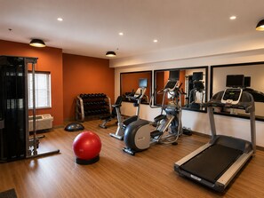 Ein Fitnessraum mit Laufbändern, Crosstrainern, Heimtrainern, einem roten Übungsball und einem Gewichthebelständer.