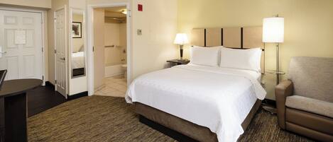 A hotel room with a bed, a desk, a chair, and a bathroom visible through an open door.