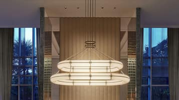 A modern hotel lobby with a central chandelier, a buffet area, and large windows offering a view of the outdoors.