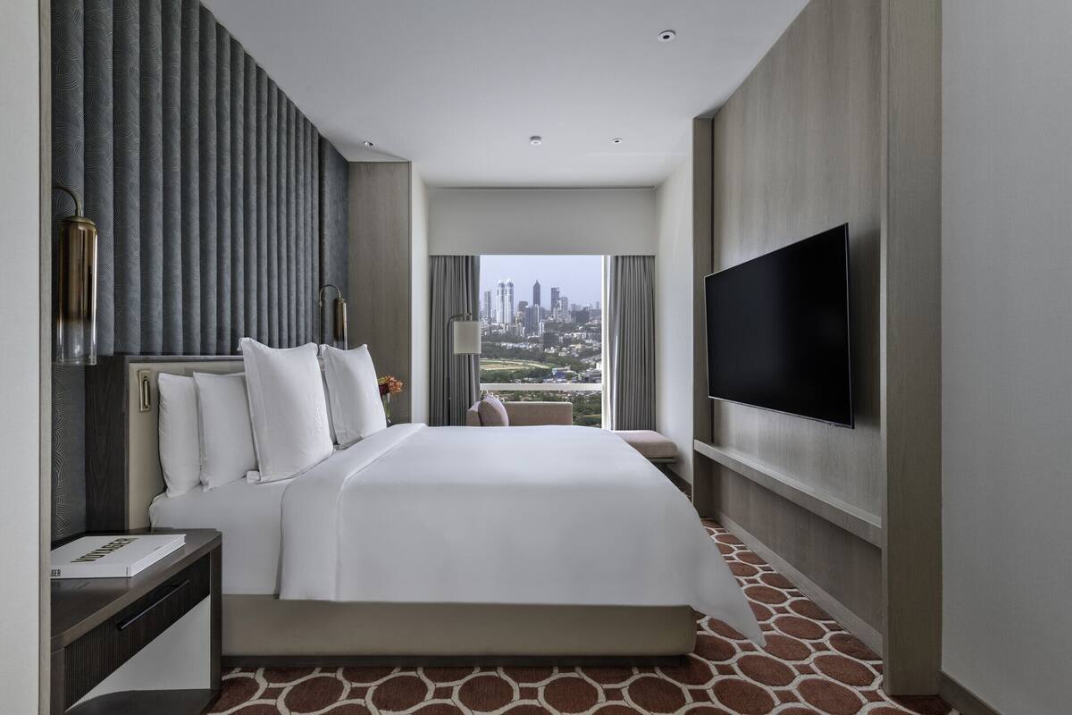 Ein Hotelzimmer mit einem großen Bett, einem Flachbildfernseher und Blick auf die Stadt.