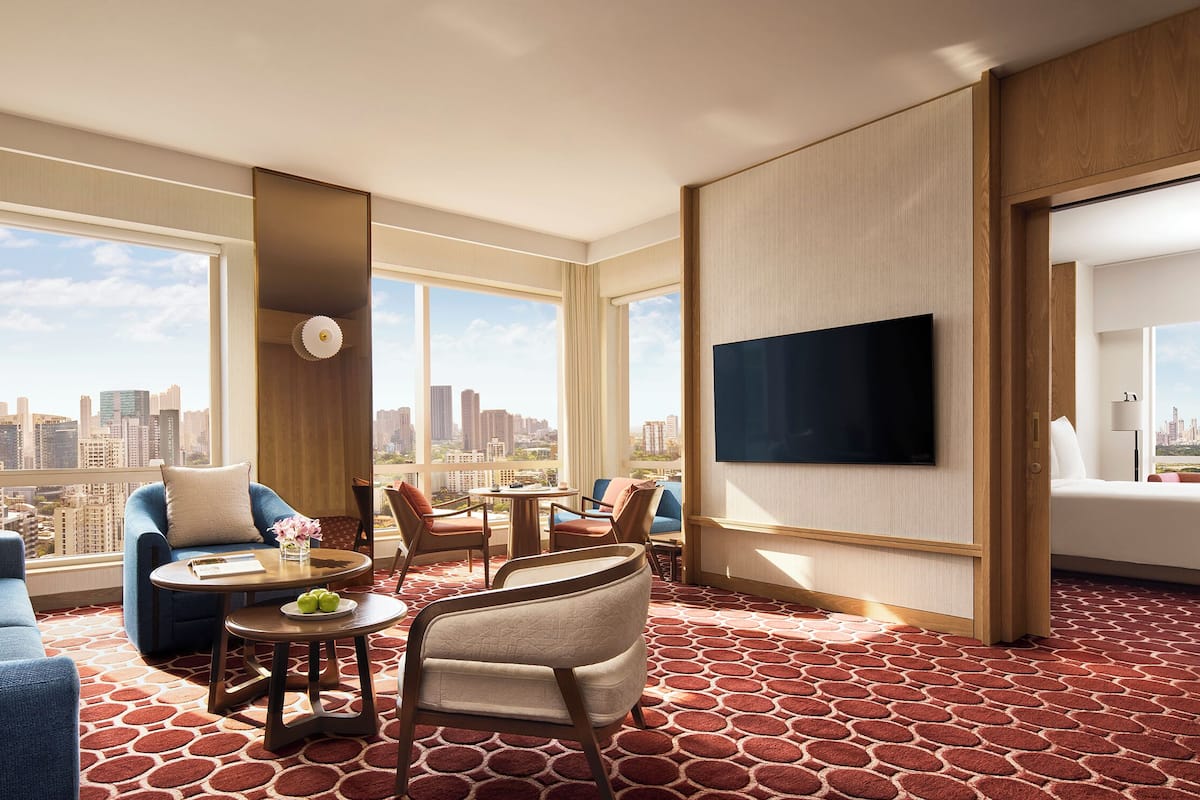 Ein Hotelzimmer mit Blick auf die Stadt, einem Flachbildfernseher, einer Sitzecke, einem Esstisch und einem gemusterten Teppich.
