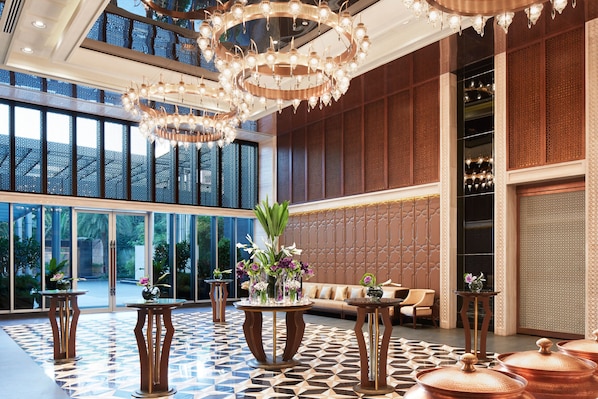 Un hall d’entrée spacieux, doté d’un sol à motifs géométriques, de plusieurs tables ornées de vases et d’un grand lustre.