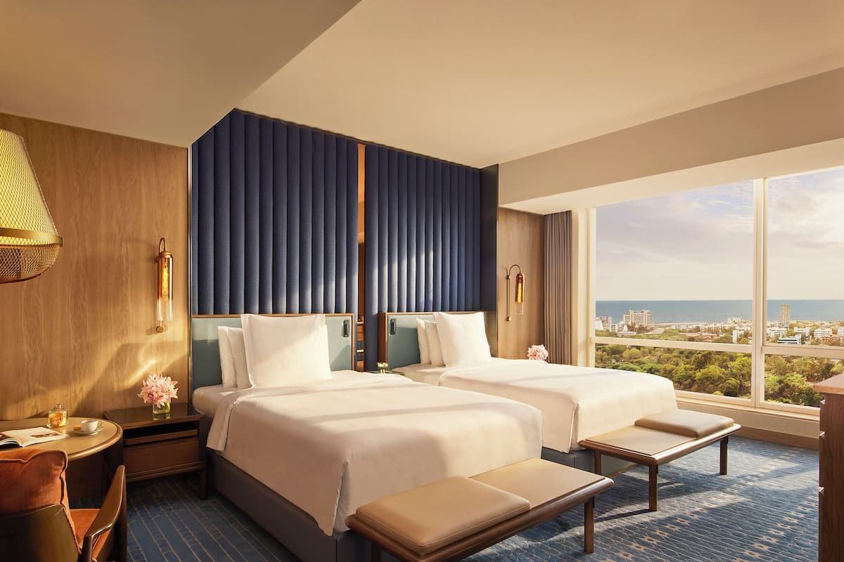 Ein Hotelzimmer mit zwei Betten, einem Schreibtisch und Blick auf die Stadt.