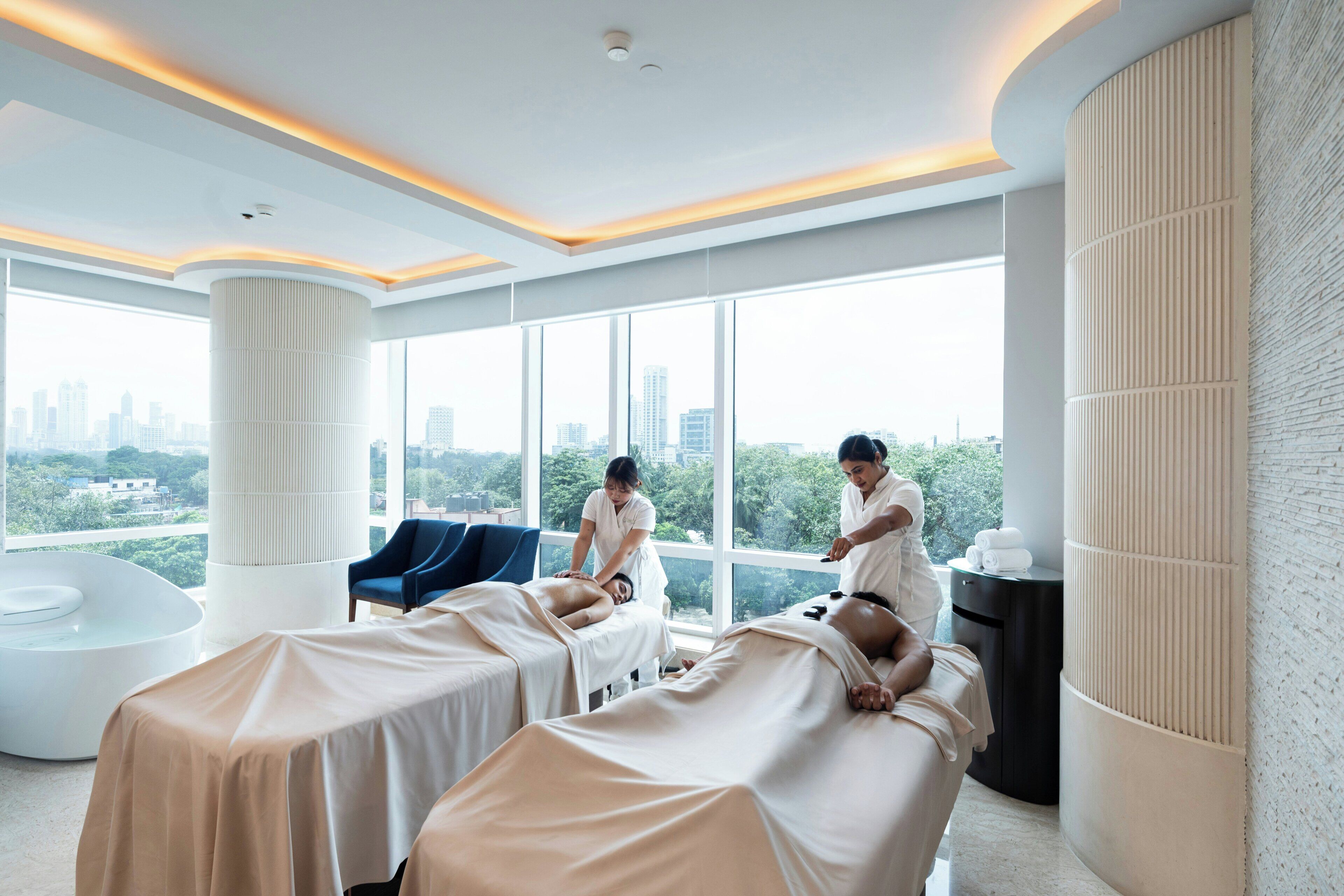 Moderni spa-huone, jossa on hierontapöytiä, hieroja ja näkymä kaupungin ylle.