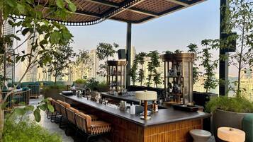 A rooftop bar with a bar counter, seating, and a view of the city skyline.
