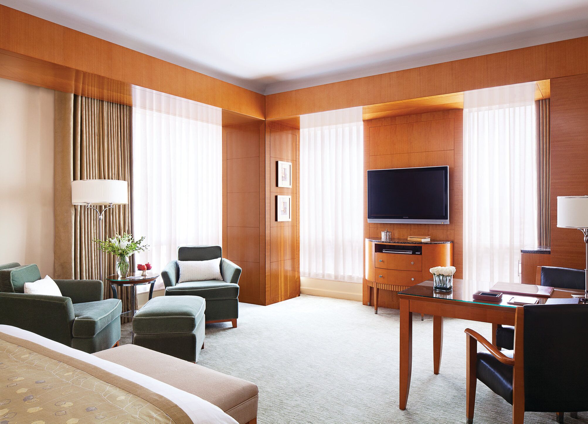 A hotel room with a flat-screen TV, a desk with a lamp, a sofa, and a chair.