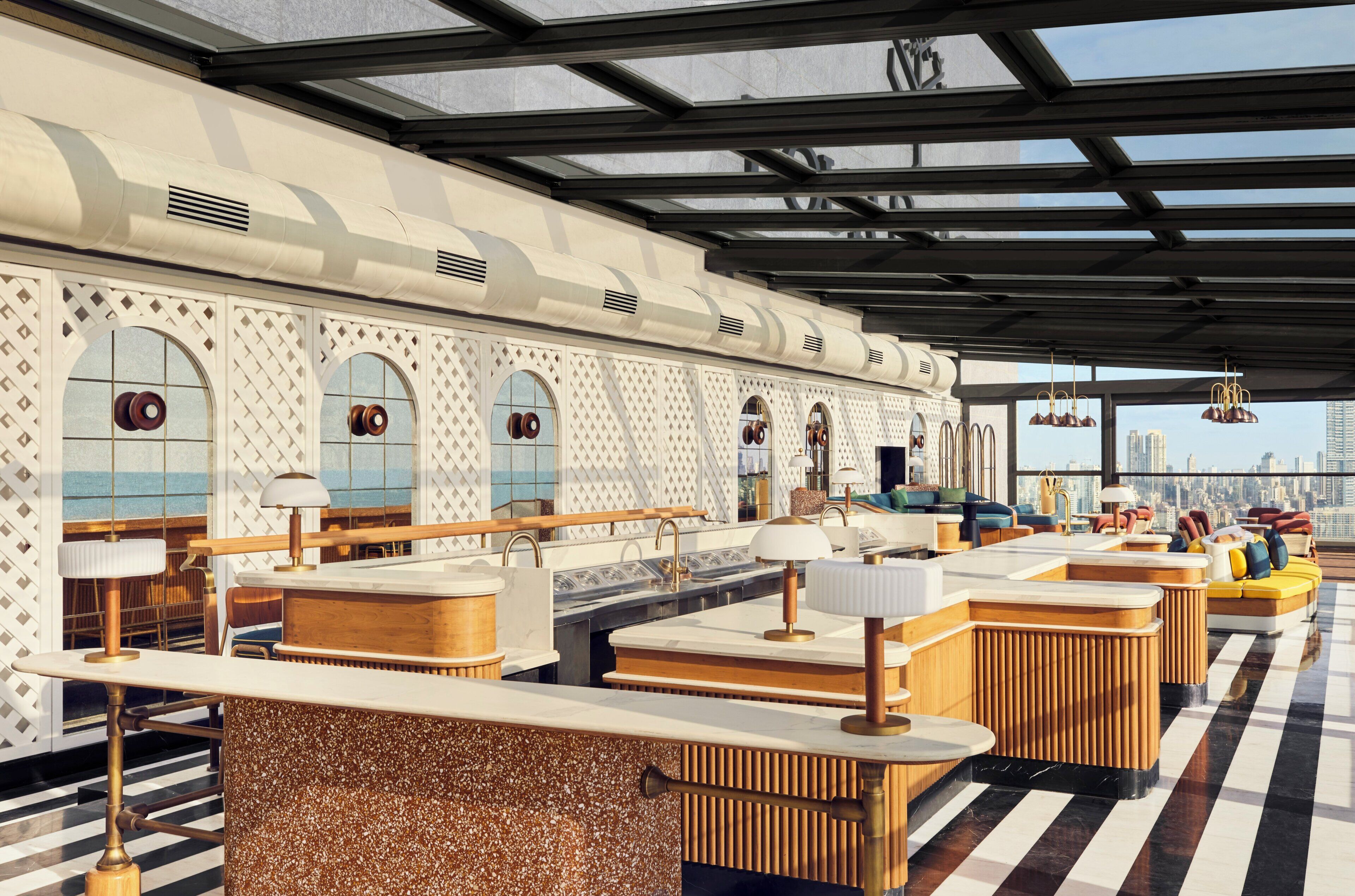 A modern interior with a long bar area, seating, and large windows offering a city view.