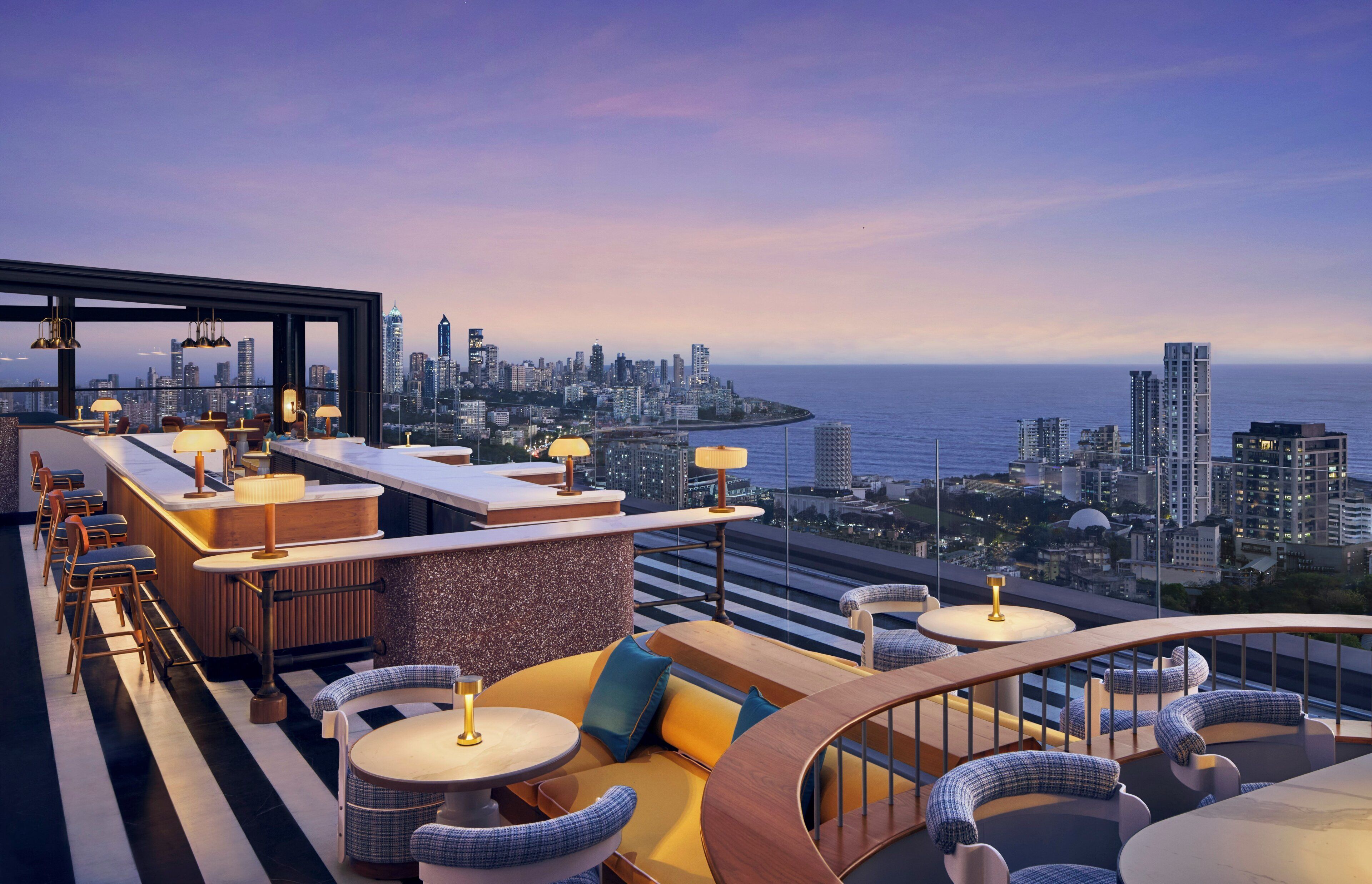 A rooftop bar with a city skyline view, seating arrangements, and a bar counter.