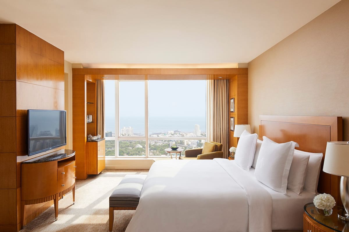Ein Hotelzimmer mit einem großen Bett, einem Fernseher, einem Schreibtisch mit Stuhl und Blick auf die Stadt durch große Fenster.