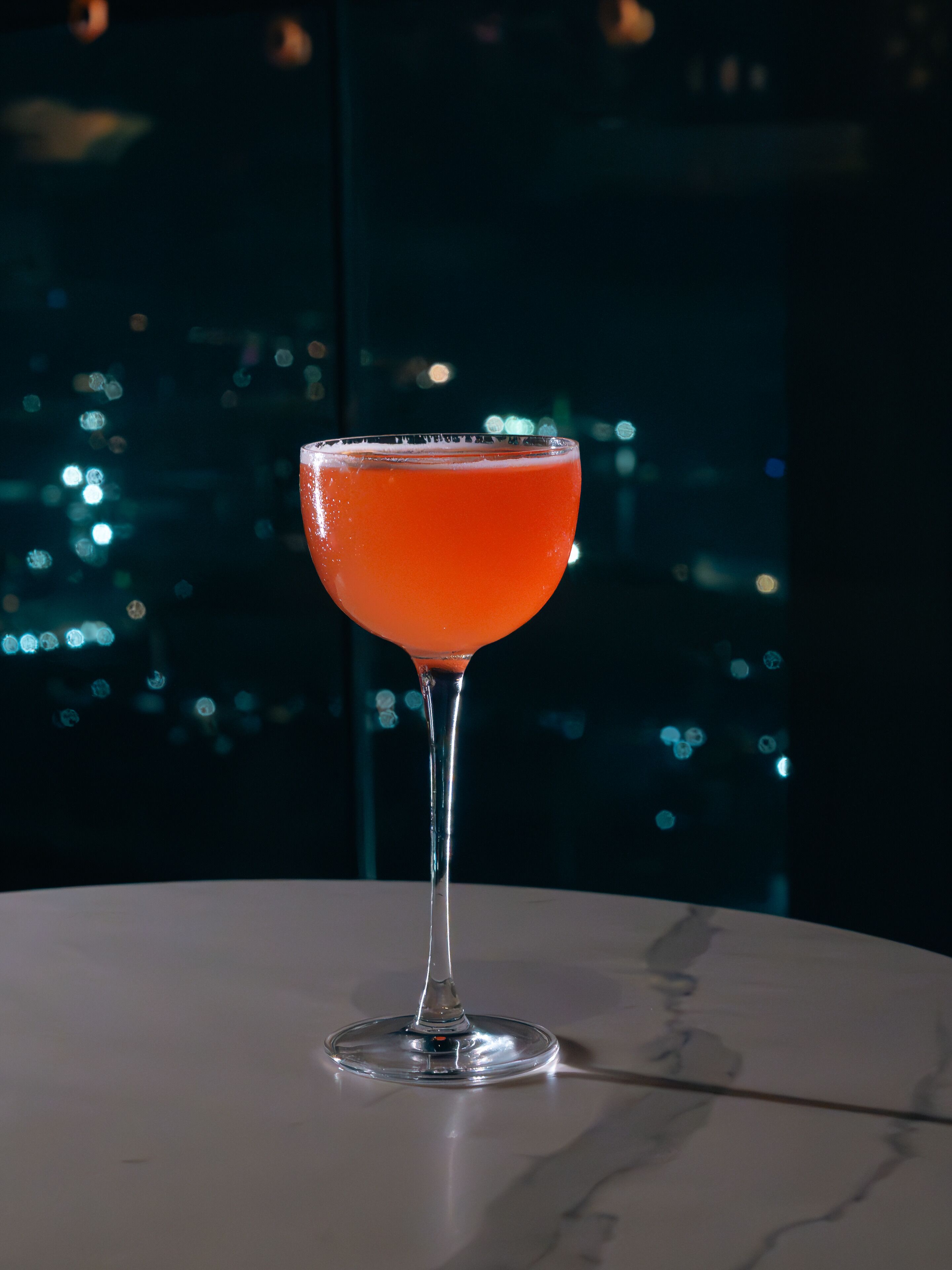 A cocktail glass on a marble table with a cityscape view in the background.