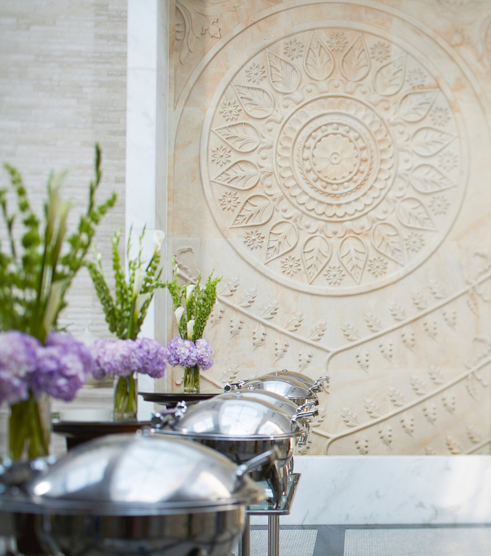 A table with silver serving dishes and a decorative wall with intricate patterns.