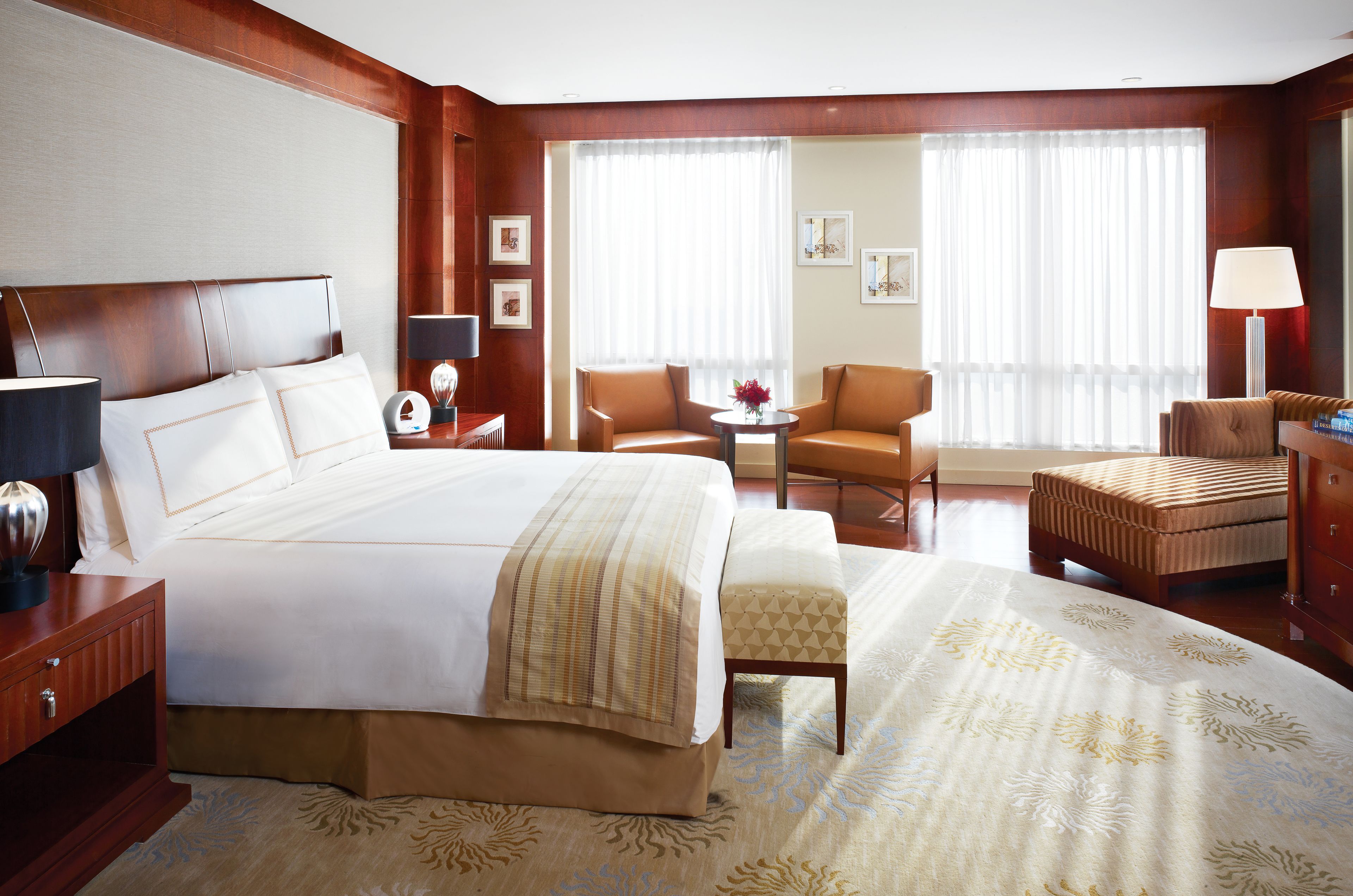 Una habitación de hotel con una cama grande, una zona de estar con mesa y sillas, y un escritorio con lámpara.