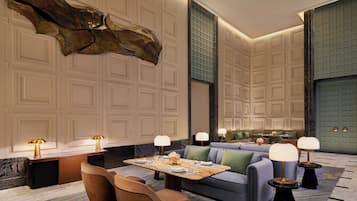 Eine moderne Hotelhalle mit Marmorboden, einer großen abstrakten Skulptur, einer Sitzecke mit Sofas und Sesseln sowie einem für zwei Personen gedeckten Esstisch.