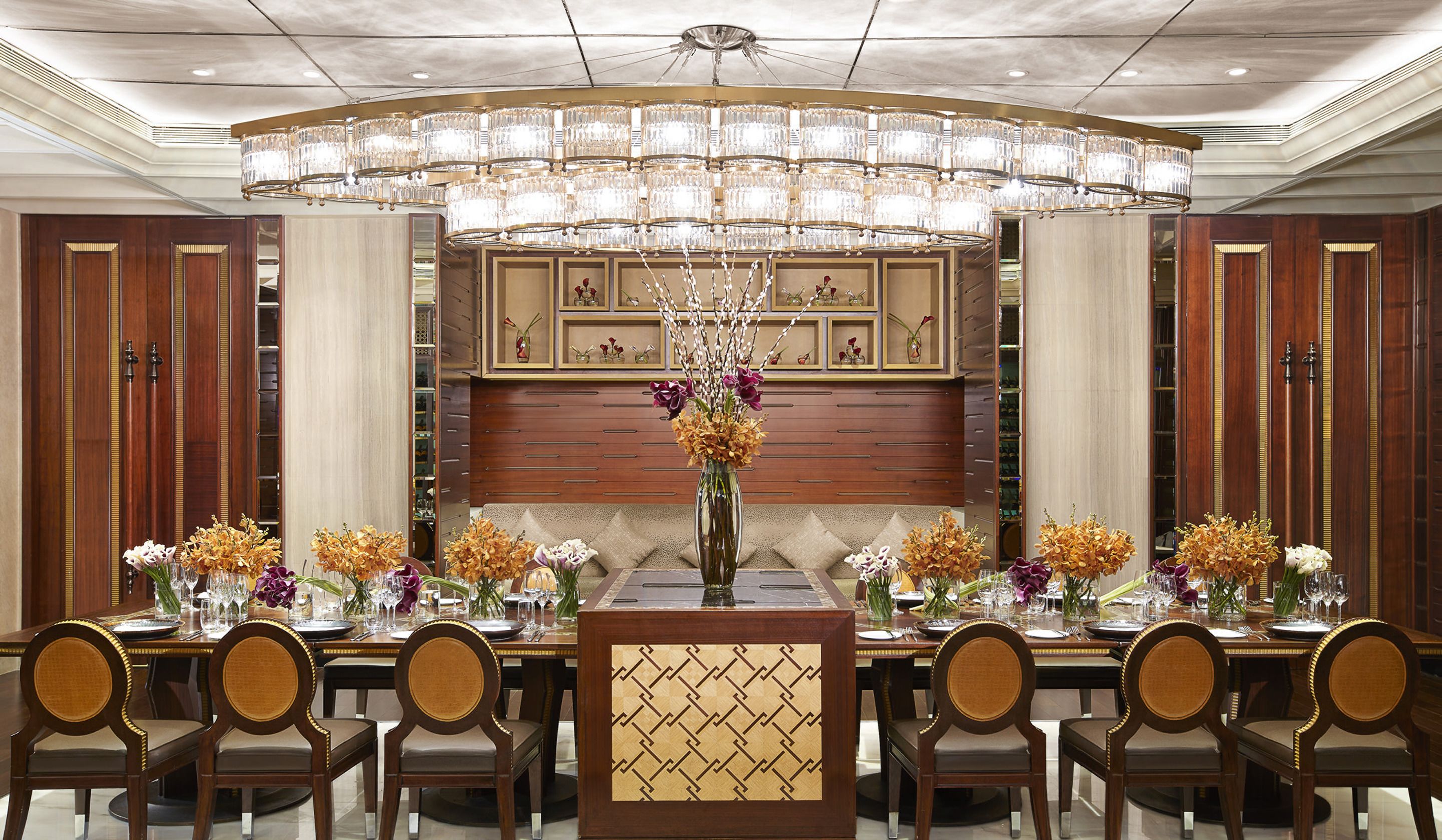 A formal dining room with a large chandelier, wooden paneling, and a long table set for multiple guests.