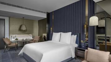 A modern hotel room with a large bed, a desk with a chair, a small table, and a mirror.