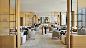 Un moderno vestíbulo de hotel con una zona de estar central, detalles de madera y ventanas amplias.