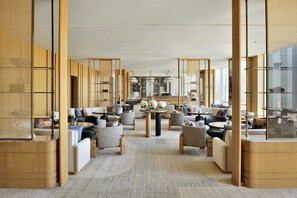 Un hall d’hôtel moderne avec un espace salon central, des éléments décoratifs en bois et de grandes fenêtres.