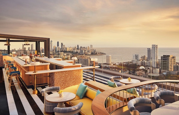 Um bar no terraço com lugares e vista para a cidade.