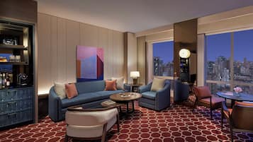 Une chambre d’hôtel moderne avec vue sur la ville, un bar et un coin salon avec une table basse et des fauteuils.