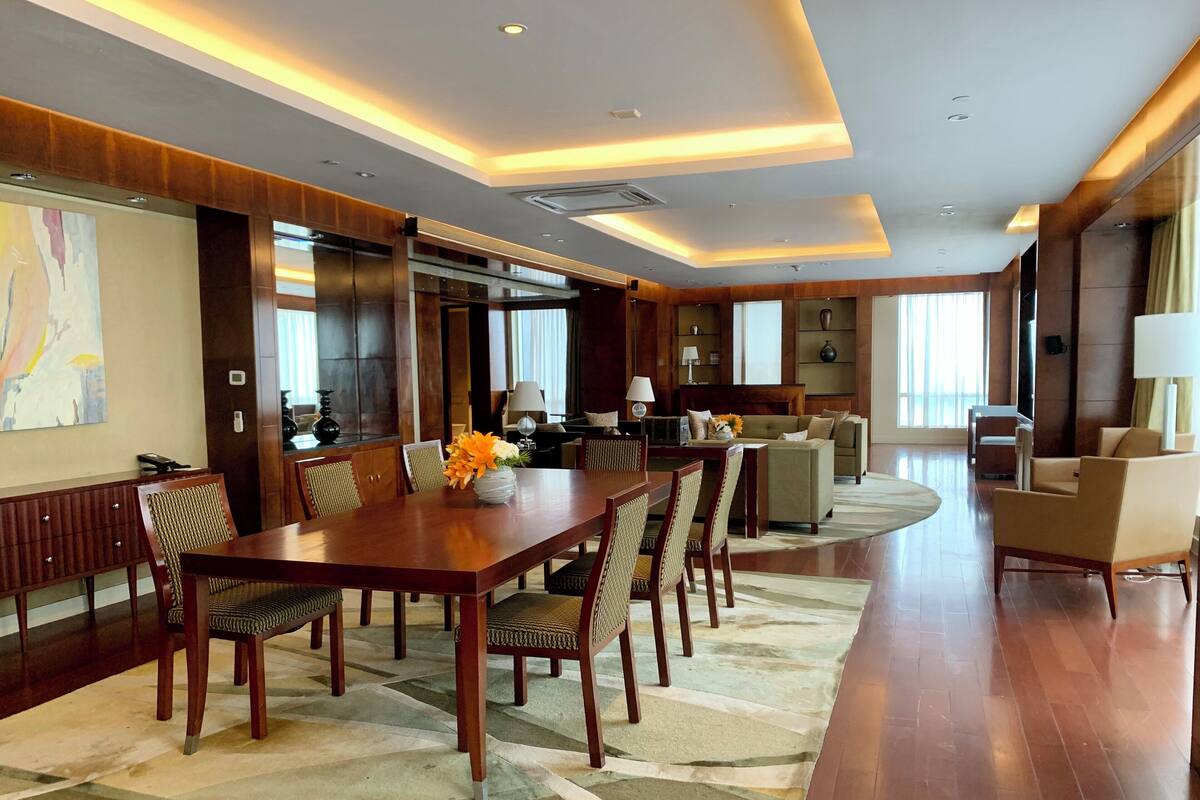 Ein geräumiges Hotelzimmer mit großem Esstisch, bequemen Sitzgelegenheiten, einer Couch und einem Fernseher.