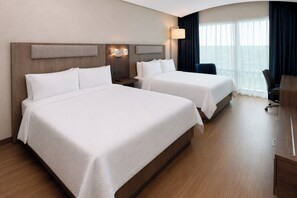 A hotel room with two beds, a desk, a chair, and a large window with curtains.