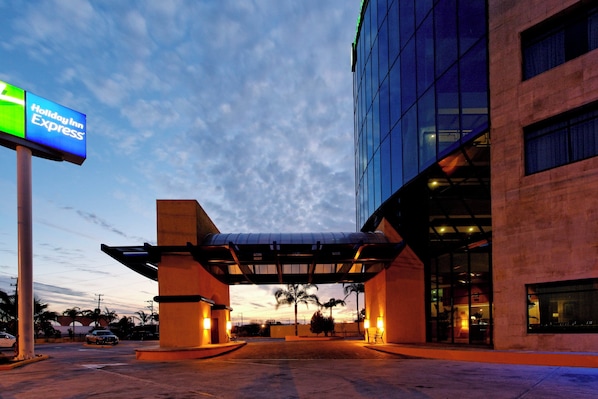 A Holiday Inn Express building with a covered entrance, palm trees, and a clear sky.