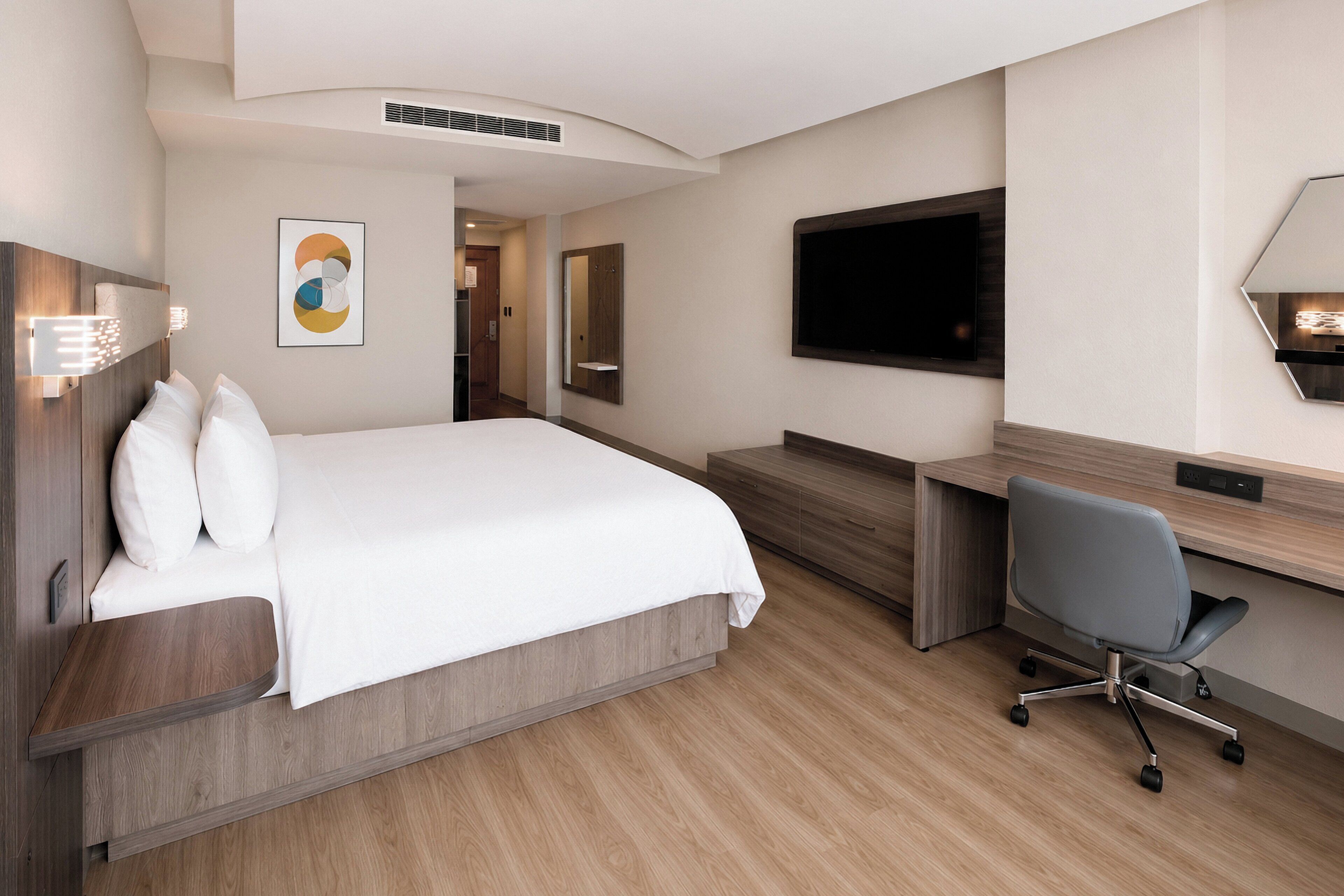 Ein Hotelzimmer mit Bett, Schreibtisch, Stuhl, Flachbildfernseher und Spiegel an der Wand.