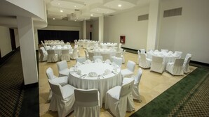 A large conference room with multiple round tables, each surrounded by chairs covered with white tablecloths and white chair covers.